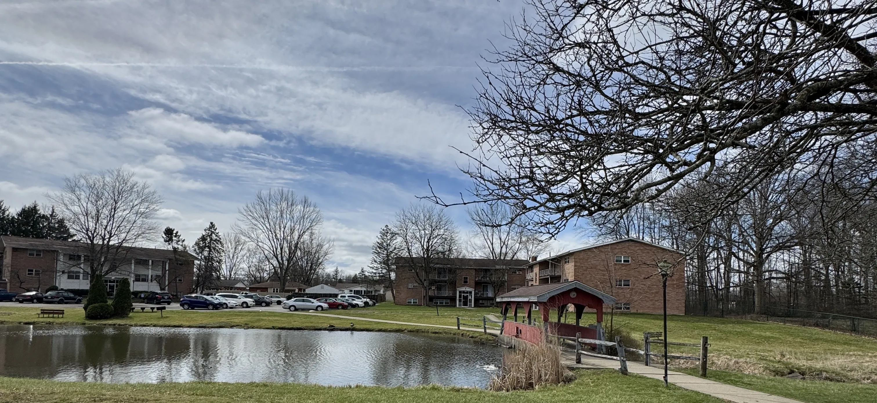 Wide view across the pond toward the covered bridge and apartment buildings under a broad sky.